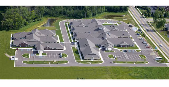 Aerial view of a single-story senior living complex with multiple connected buildings, parking areas, driveways, and surrounding lawns.