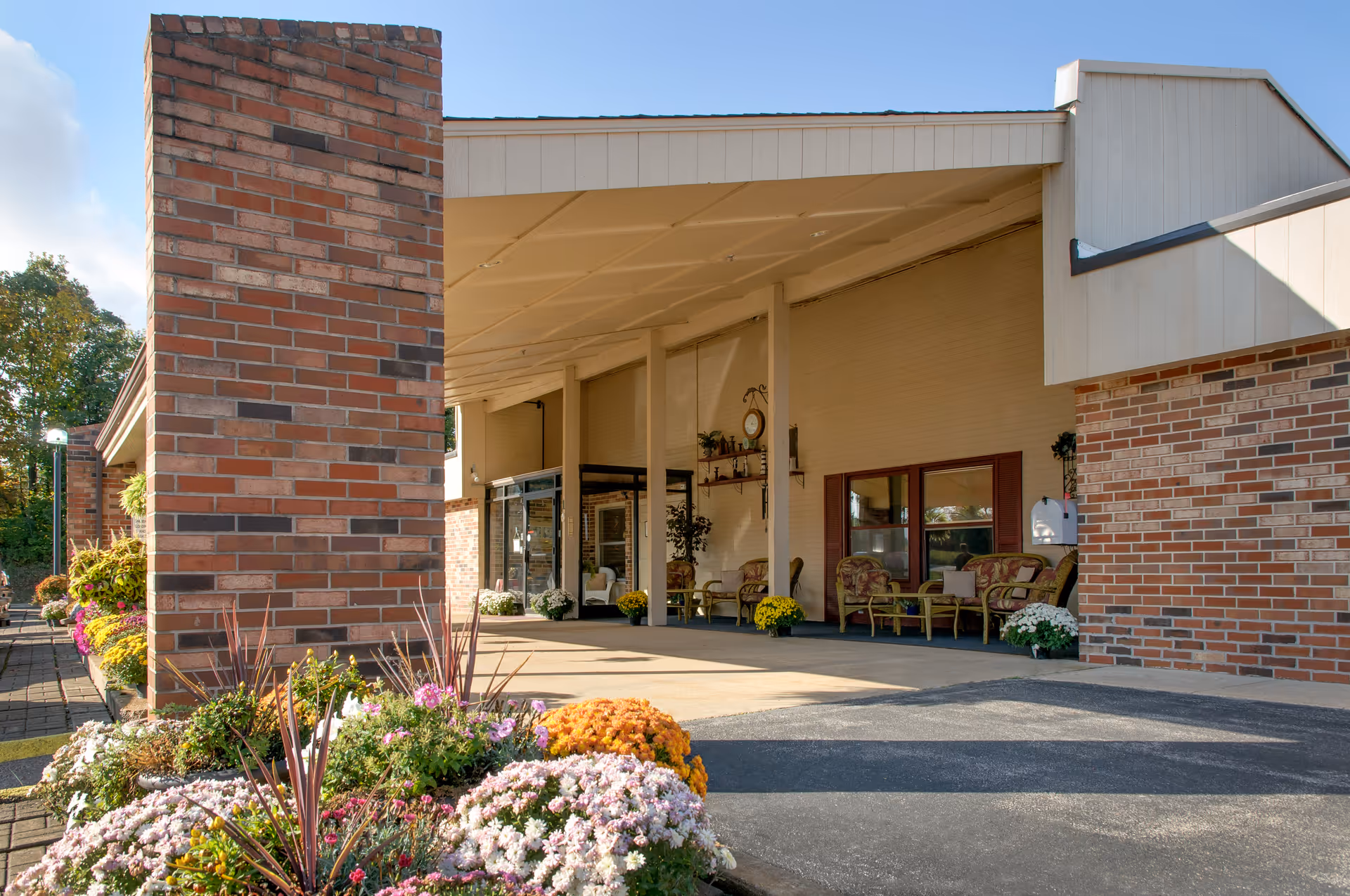 Covered entrance of the Life Care Center of Sullivan with brick pillars, colorful flower beds, and outdoor seating under a canopy.