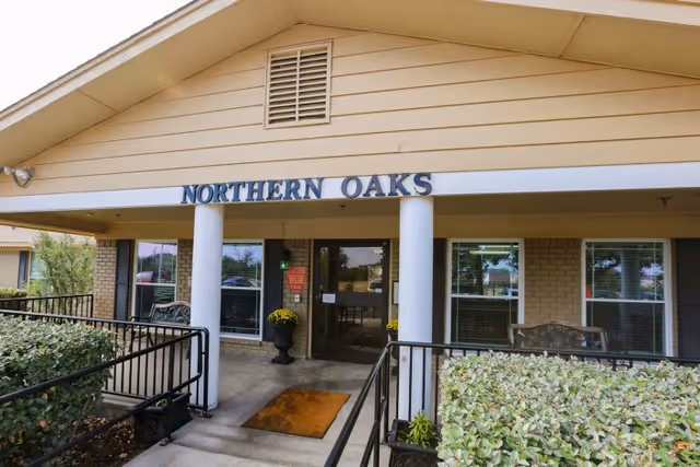 Front entrance of Northern Oaks Living & Rehabilitation Center with a covered porch, columns, ramps, and the facility sign above the doorway.