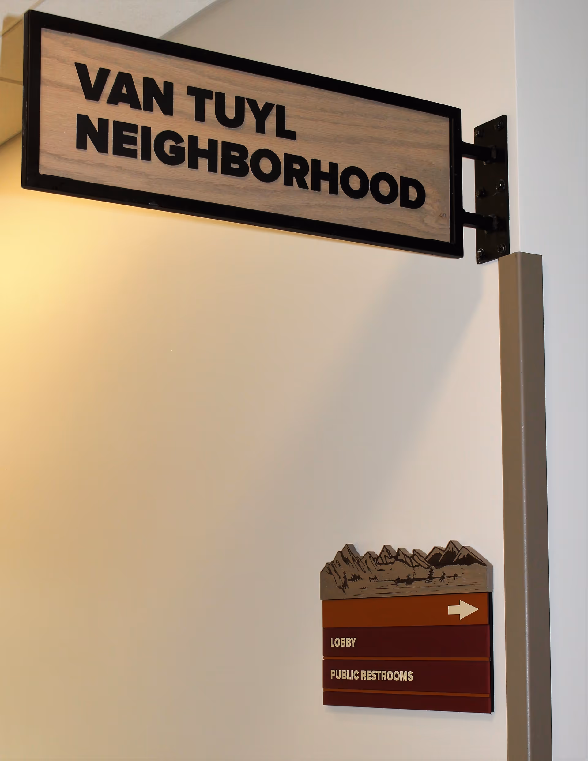 Wall-mounted indoor sign reading 'VAN TUYL NEIGHBORHOOD' with a small directional plaque indicating 'Lobby' and 'Public Restrooms'.