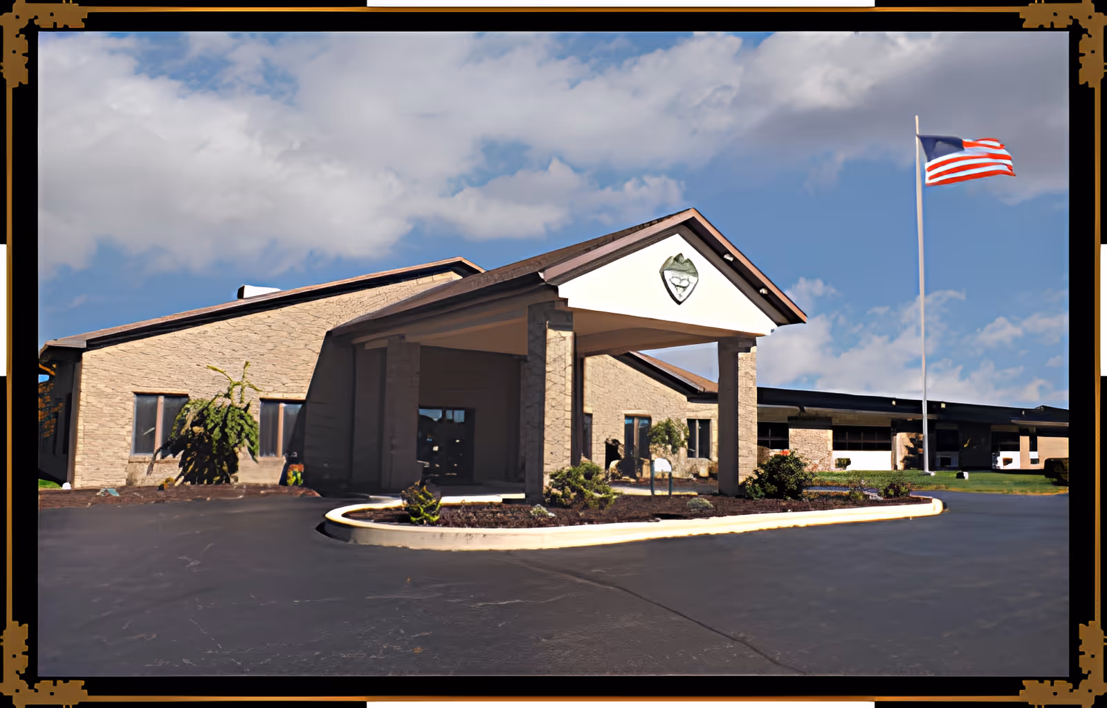 Front entrance of a single-story senior living facility with a covered porte-cochère and an American flag flying on a flagpole.