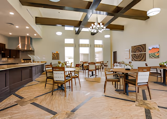 Spacious dining room with multiple tables and chairs, high beamed ceiling, and a serving counter on the left.