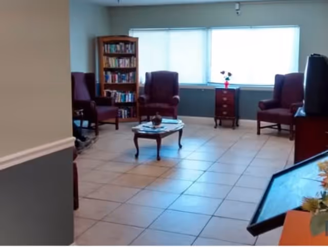 Small sitting room with armchairs, a coffee table, a bookcase and a large window in a senior living facility.