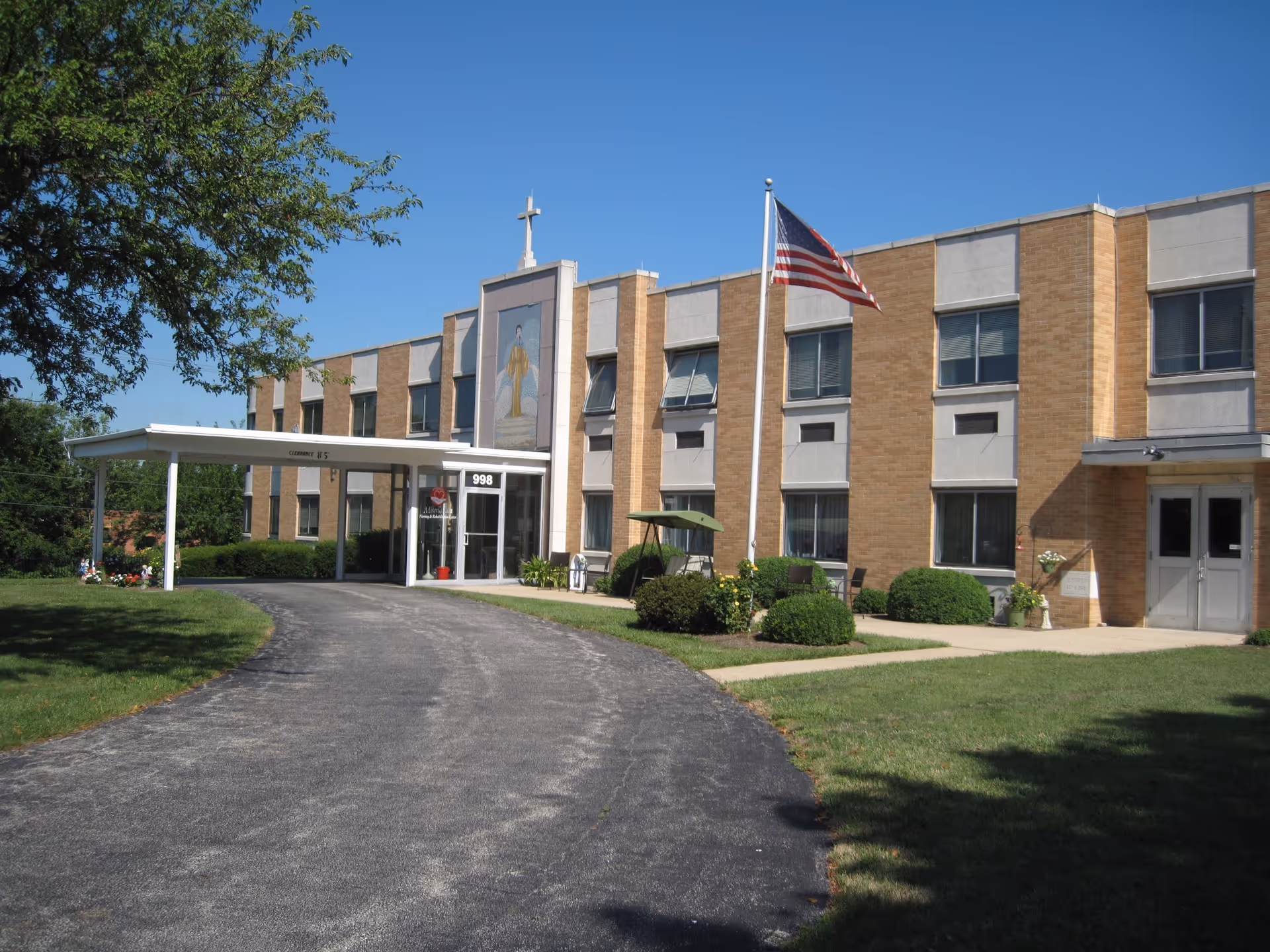 Front exterior of a two-story brick nursing and rehabilitation center with a covered entrance, American flag, and driveway.