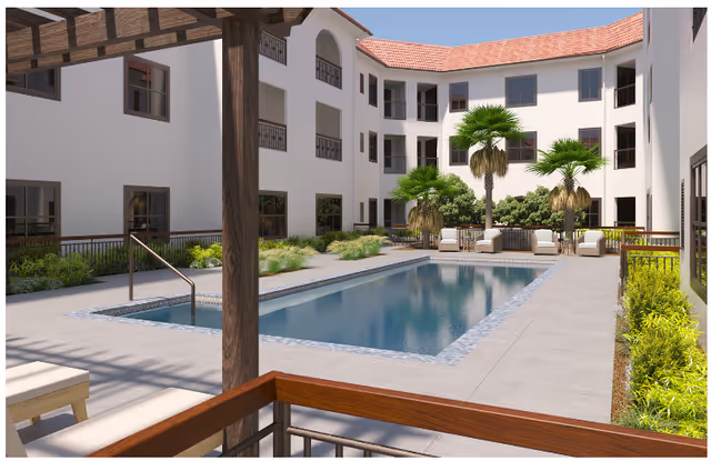 Outdoor courtyard area of The Hacienda Mission San Luis Rey featuring a rectangular swimming pool surrounded by a concrete deck, palm trees, shrubs, and lounge chairs. The courtyard is enclosed by a three-story building with white walls and red tile roofing.