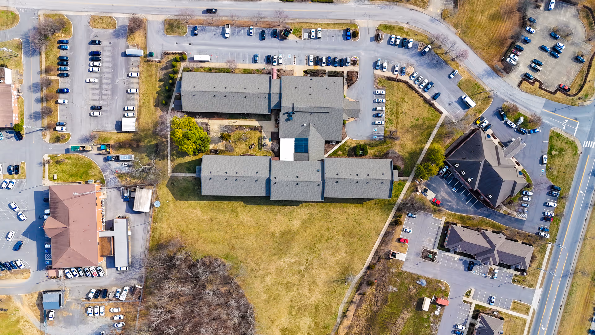 Aerial view of a retirement community complex with connected buildings, parking lots, lawns, and surrounding roads.