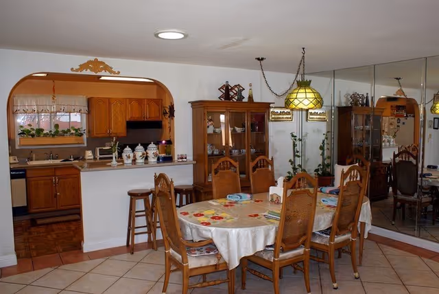 Dining room with a round table, wooden chairs, and a kitchen pass-through arch.