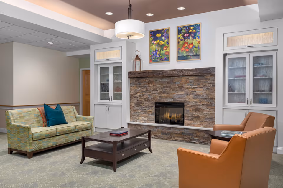Cozy lounge area with a patterned sofa, two armchairs, a coffee table and a stone fireplace beneath colorful artwork.