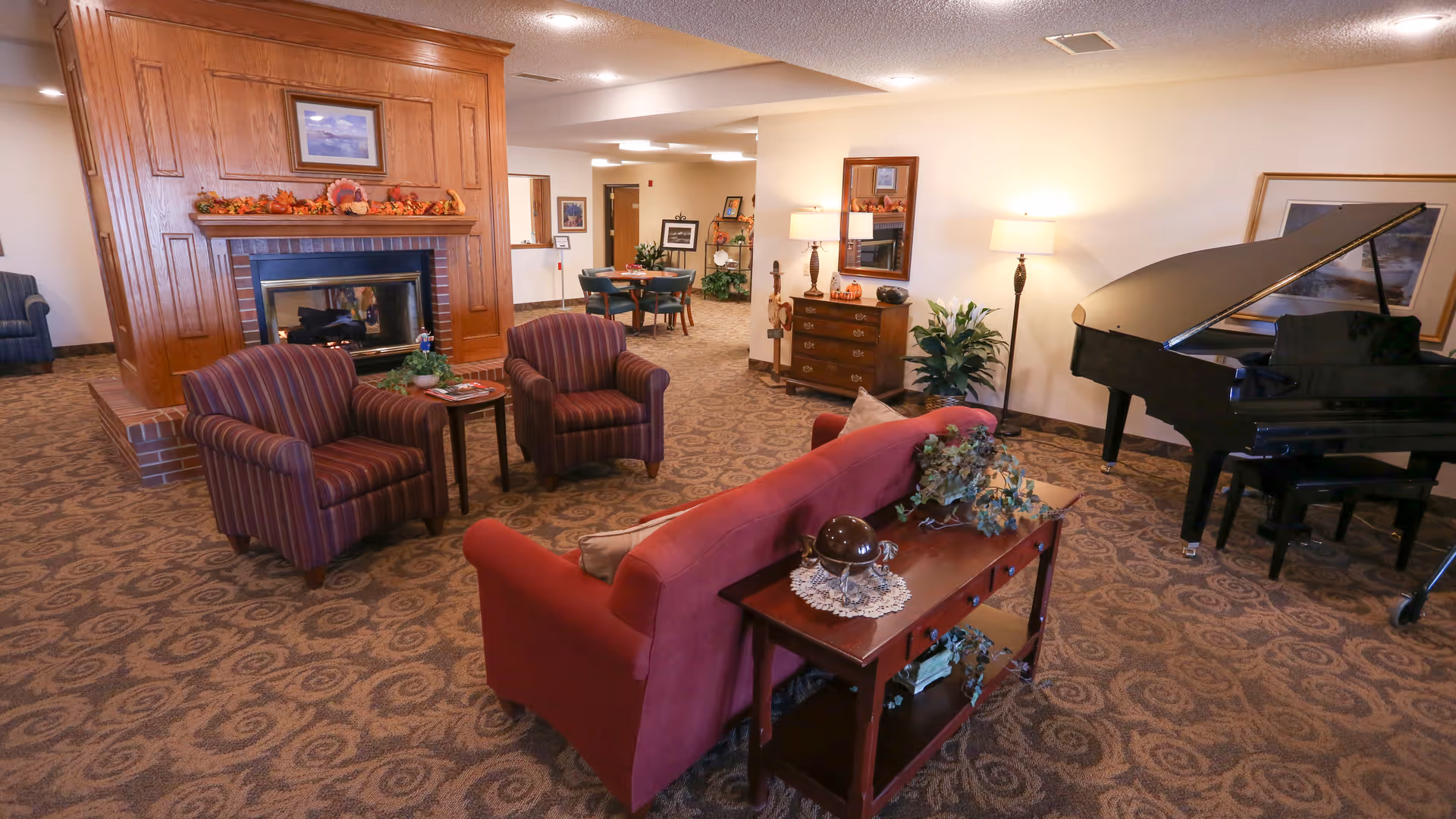 Spacious communal lounge with upholstered seating arranged around a fireplace and a grand piano.