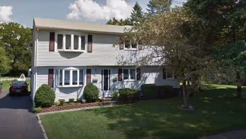 Two-story Caroline Manor building with white siding, red shutters, and a manicured front yard.