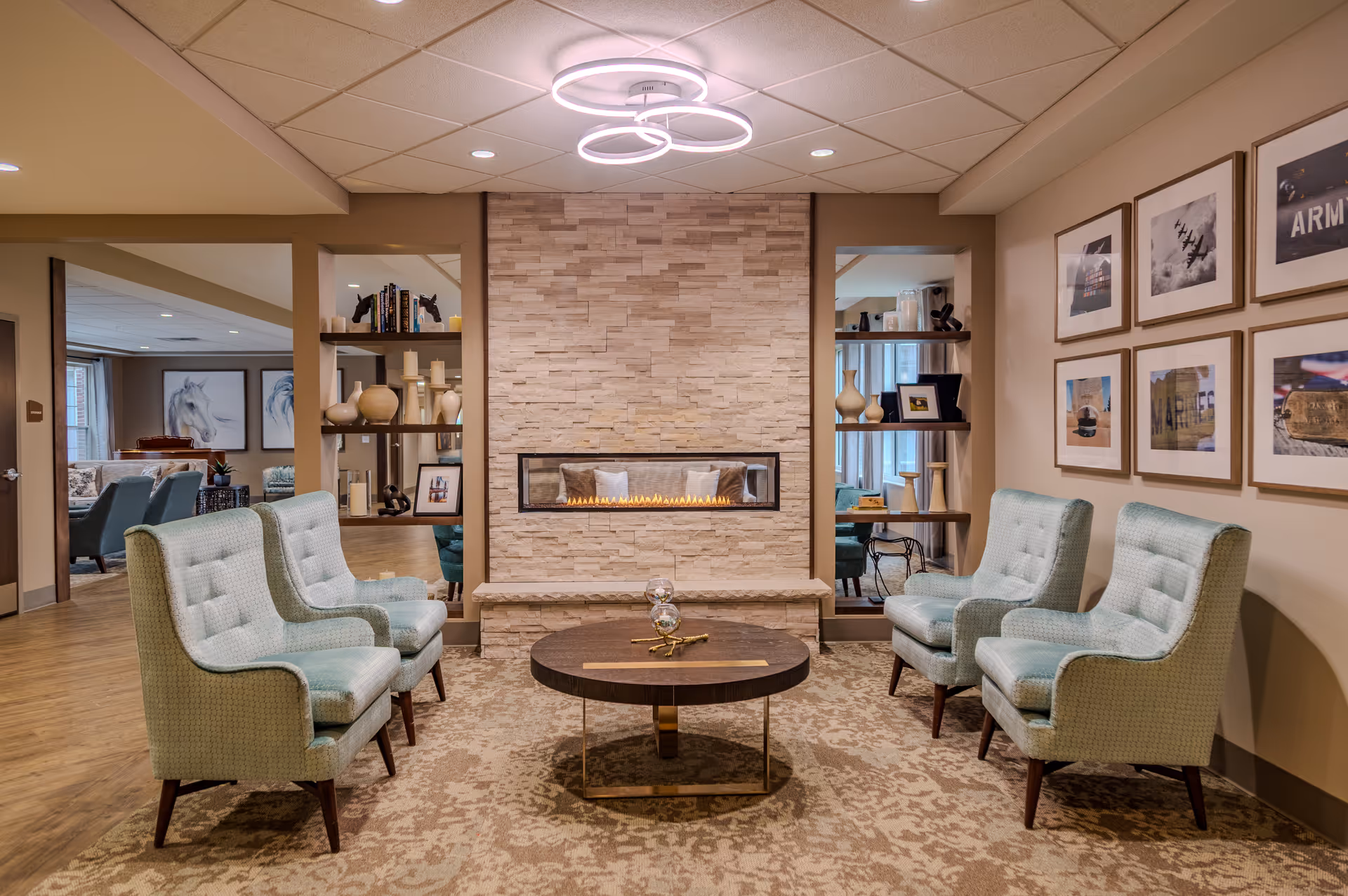 Lounge area with four upholstered armchairs around a round coffee table facing a modern linear fireplace set in a stone wall.
