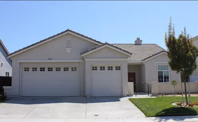 Residential-style facility exterior with a two-car garage and neatly trimmed lawn.