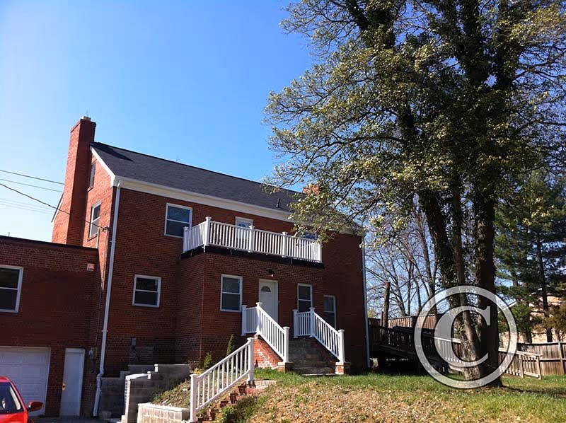 Brick two-story building with a front porch, stairs, and surrounding lawn.