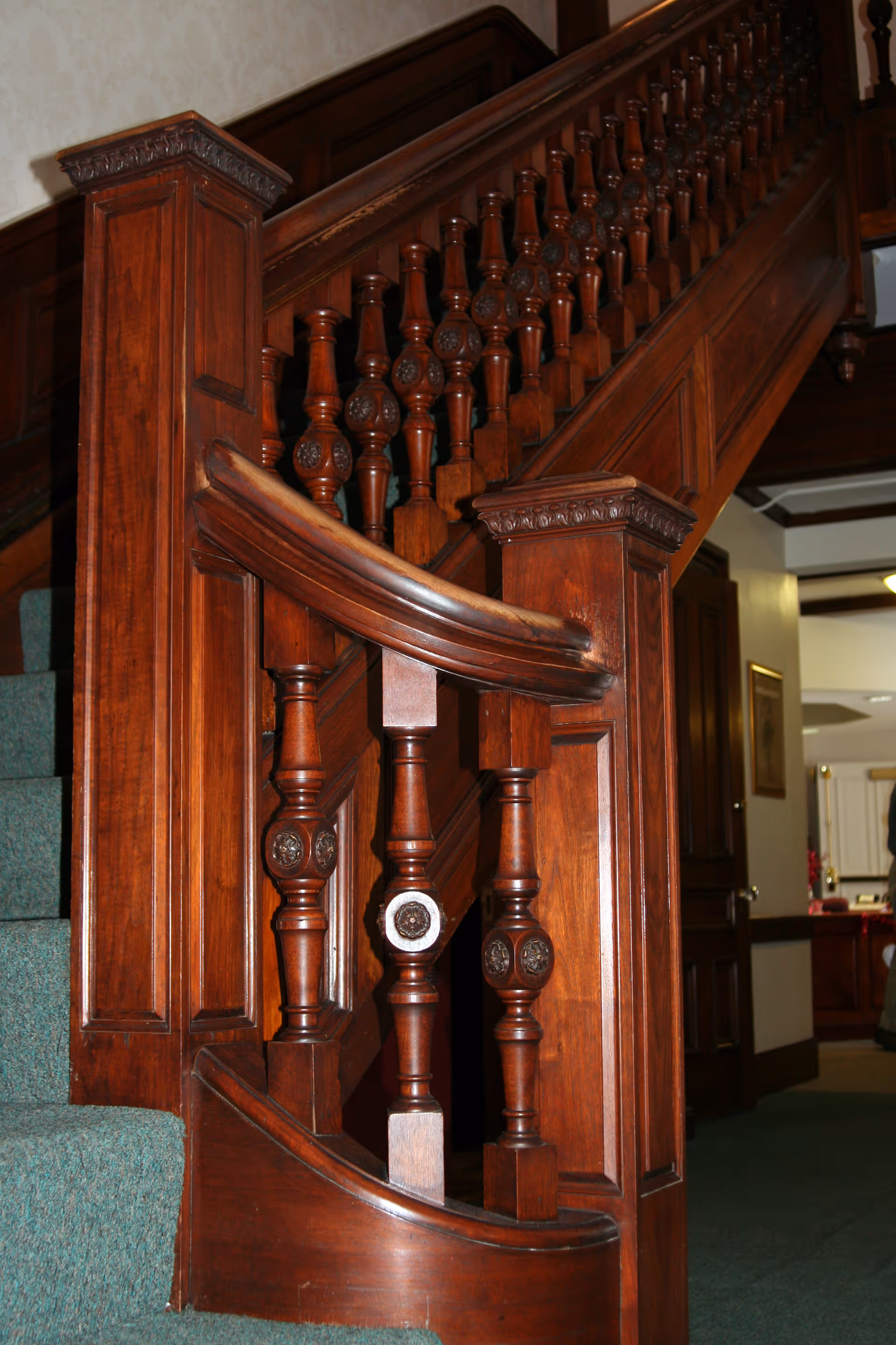Ornate polished wooden staircase banister with carved balusters in an interior hallway.