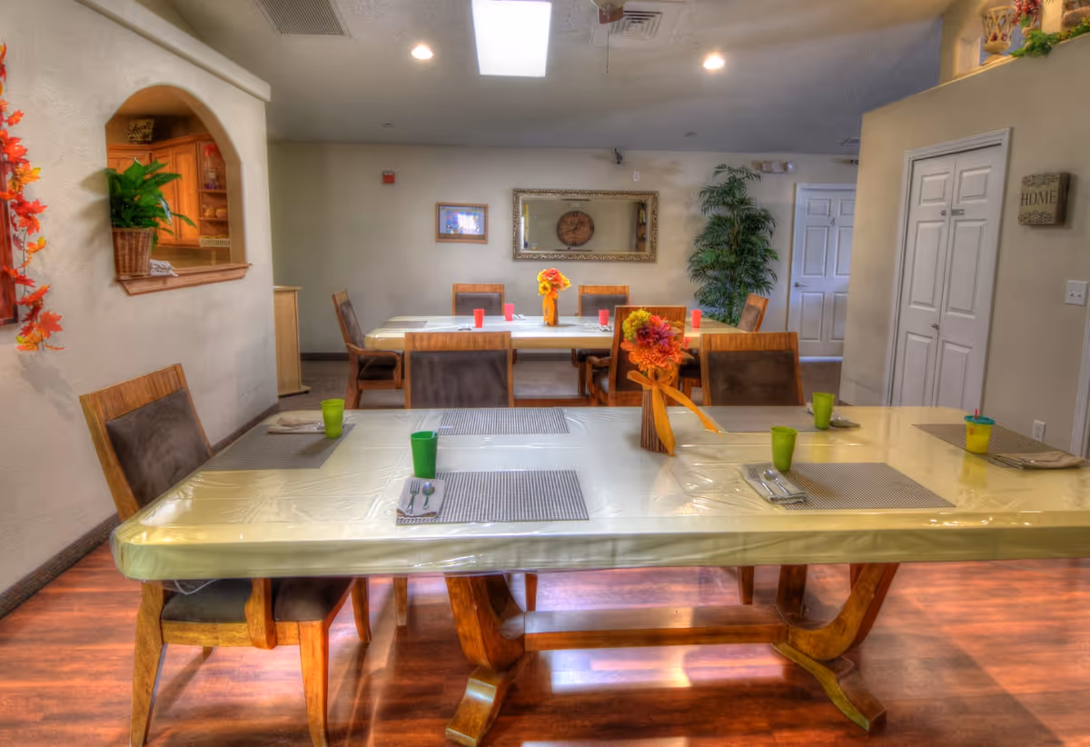 A cozy dining room with long tables, chairs, and fall centerpieces in a senior facility.