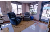 Two blue recliners in a sunlit living room with windows and a glass door.
