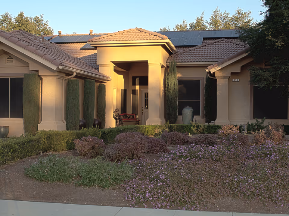 Front exterior of a single-story stucco residence with a tiled roof, columned entryway, and landscaped front garden.