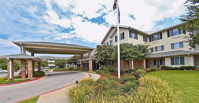 Front exterior of Morada Broken Arrow senior living building with a covered porte-cochere, flags, and landscaped lawn.