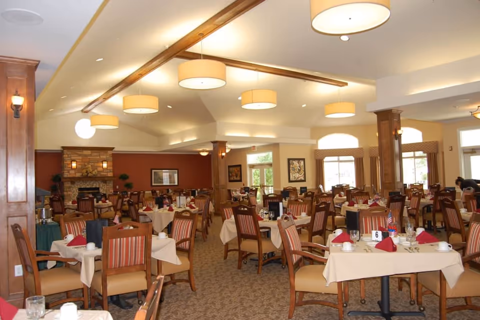 Spacious dining room with many set tables and wooden chairs, pendant lights overhead, and a stone fireplace at the far end.
