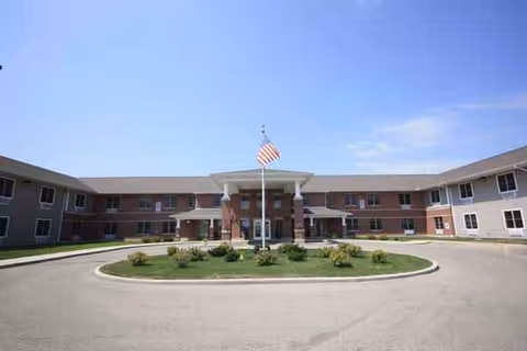 A brick senior living facility with a circular driveway, flagpole, and landscaped central island.