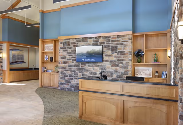 Reception desk and lobby with a stone accent wall, wall-mounted TV reading Shorehaven, and built-in wooden shelving.