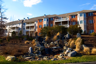 Three-story senior living building with balconies and a landscaped rock garden.