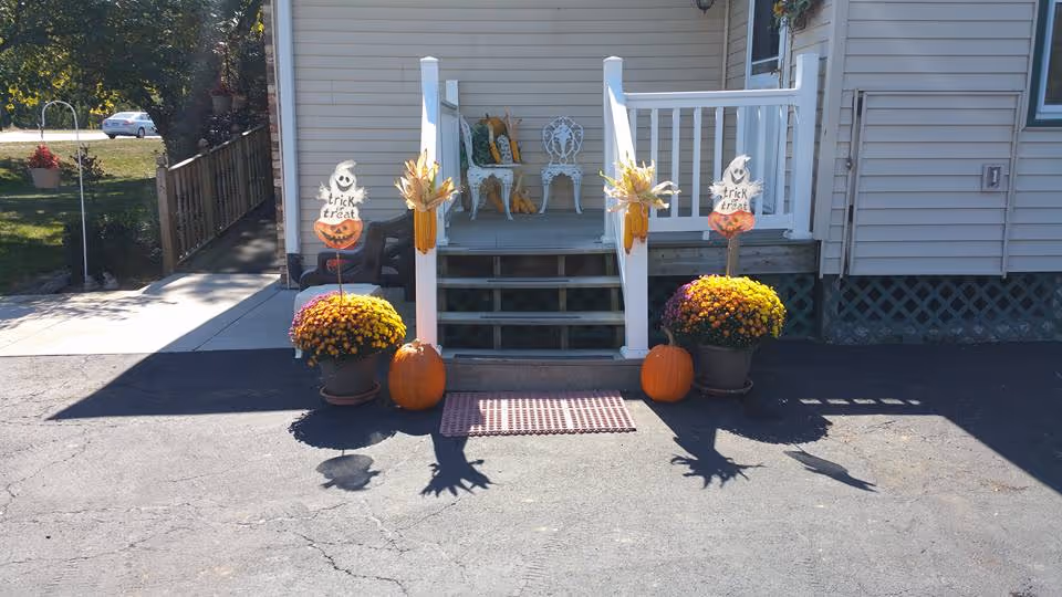 Small front porch with steps decorated for fall with pumpkins, potted mums, corn stalks and Halloween 'trick or treat' signs.