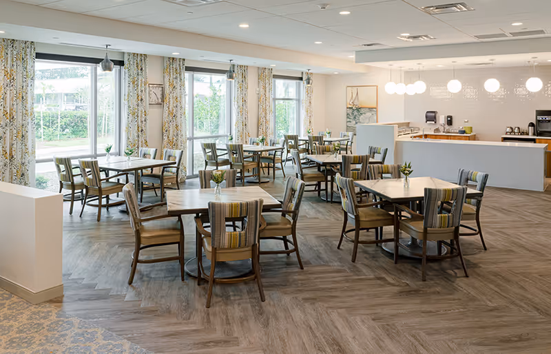 Bright, spacious dining room with multiple tables and chairs, large windows, and a serving counter.
