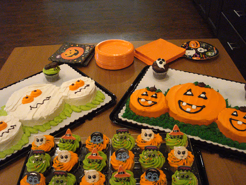 An assortment of Halloween-themed cakes and cupcakes arranged on a wooden dining table.
