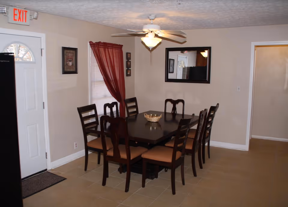 A dining room with a dark table and eight chairs, beige walls, and a ceiling fan.