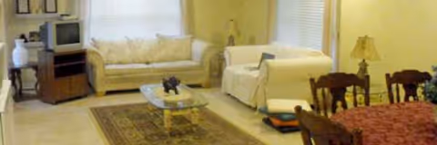 A spacious senior living room with beige sofas, a glass coffee table, and a TV stand.