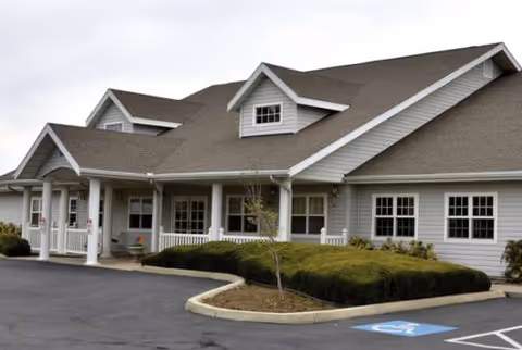 Front view of a senior living facility with a covered entrance and wheelchair-accessible parking.