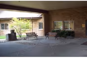 Outdoor covered walkway with brick building, benches, and a small tree.