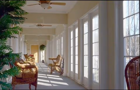 Sunlit interior corridor at Caremoor Retirement Center with windows, wicker seating, and ceiling fans.