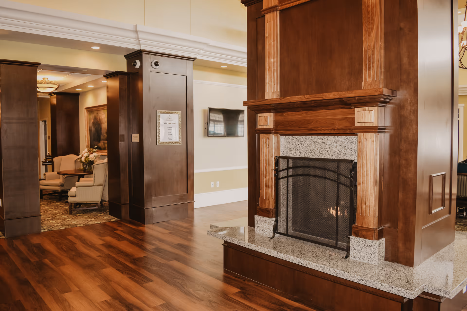 Spacious common area with a large wooden fireplace, hardwood floors, and seating visible in the background.