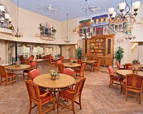 Sunny dining room with round wooden tables, red chairs, chandeliers, and mural walls.
