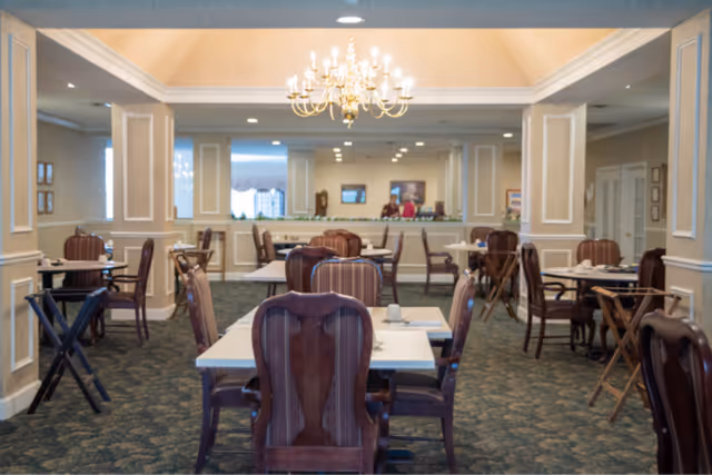 Spacious formal dining room with multiple tables and upholstered chairs and a central chandelier.