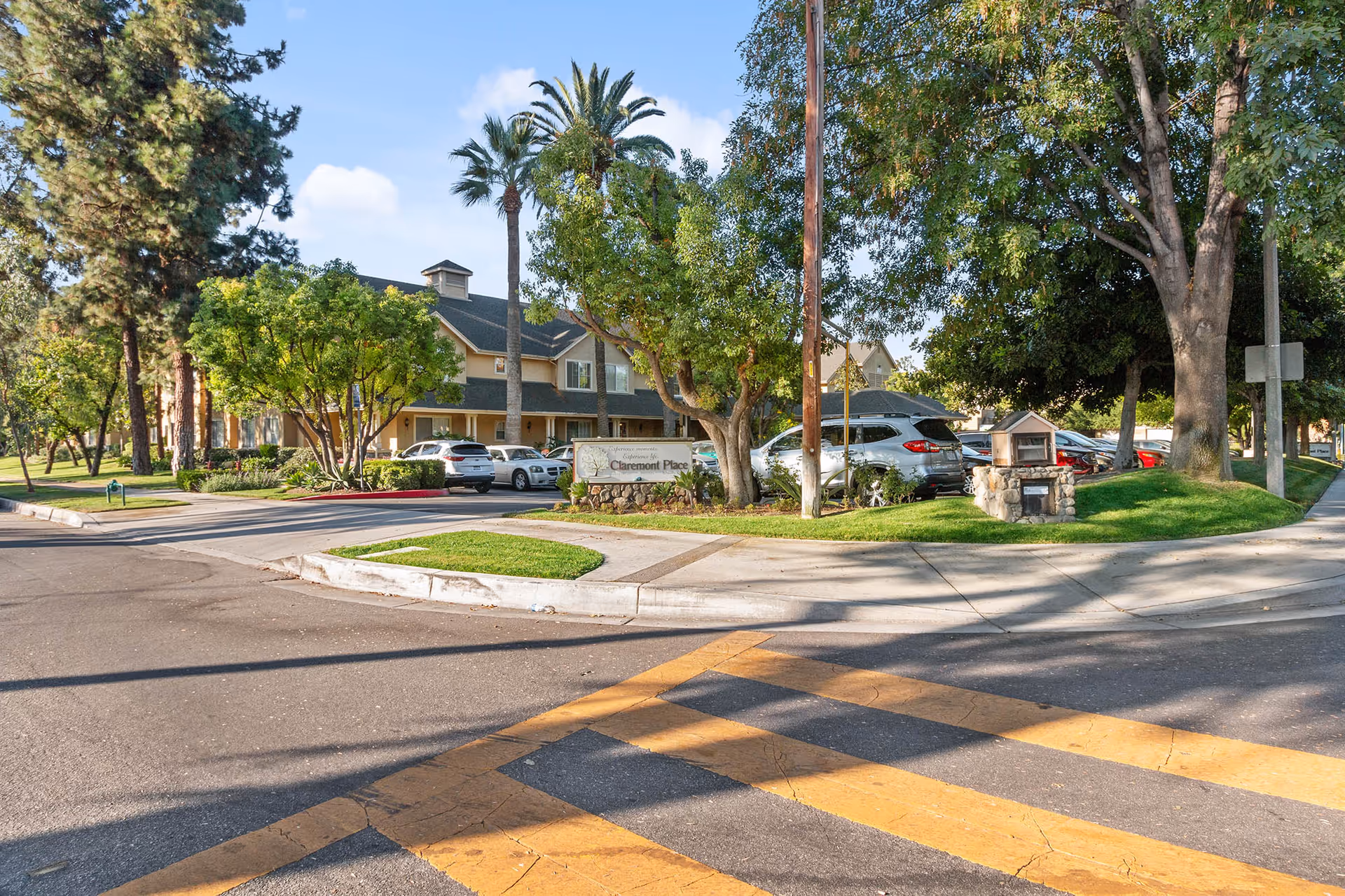 Exterior view of Claremont Place senior living building with trees, parked cars, and an entrance sign at a street corner.