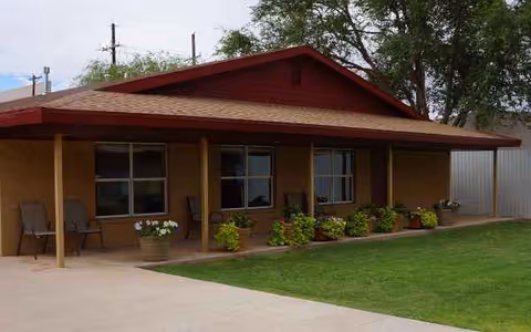 Single-story tan building with a red gable roof, covered porch, and potted plants outside.