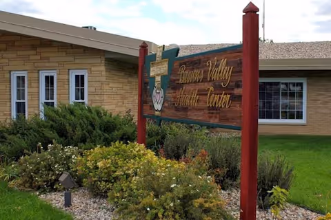 A wooden sign reading 'Browns Valley Health Center' stands among shrubs in front of a single-story brick building.