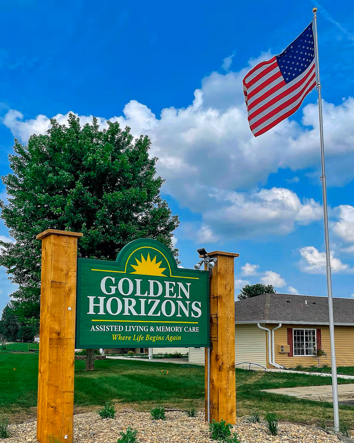 Entrance sign reading "Golden Horizons" for an assisted living and memory care facility on a lawn with an American flag and the building in the background.