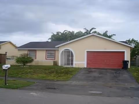 Front view of a single-story beige building with curved entry arch and red garage door.