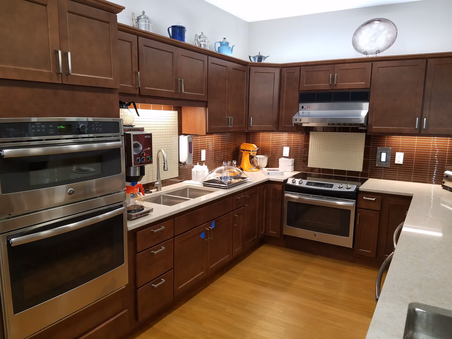 Well-equipped kitchen with dark wood cabinets, stainless steel double ovens and stove, a sink, and countertop appliances.