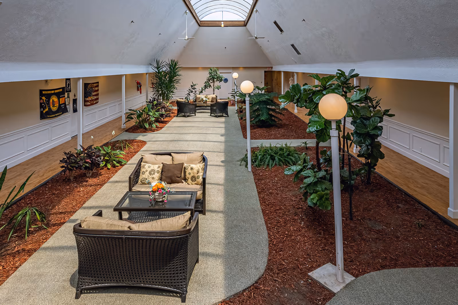 Indoor atrium-style common area with wicker seating, plants, globe lamps and a skylight.