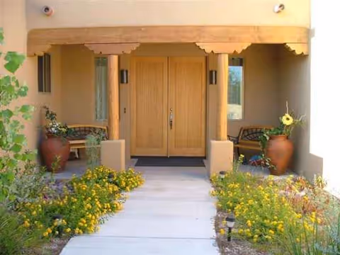Front entrance of a care home with double doors, benches, and potted plants.