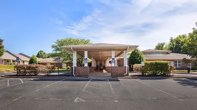 Front entrance of a senior living facility with a covered porte-cochère, brick columns, accessible parking spaces, and landscaping.