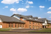 Exterior view of a large brick building with multiple windows and a sloped roof under a blue sky with scattered clouds.