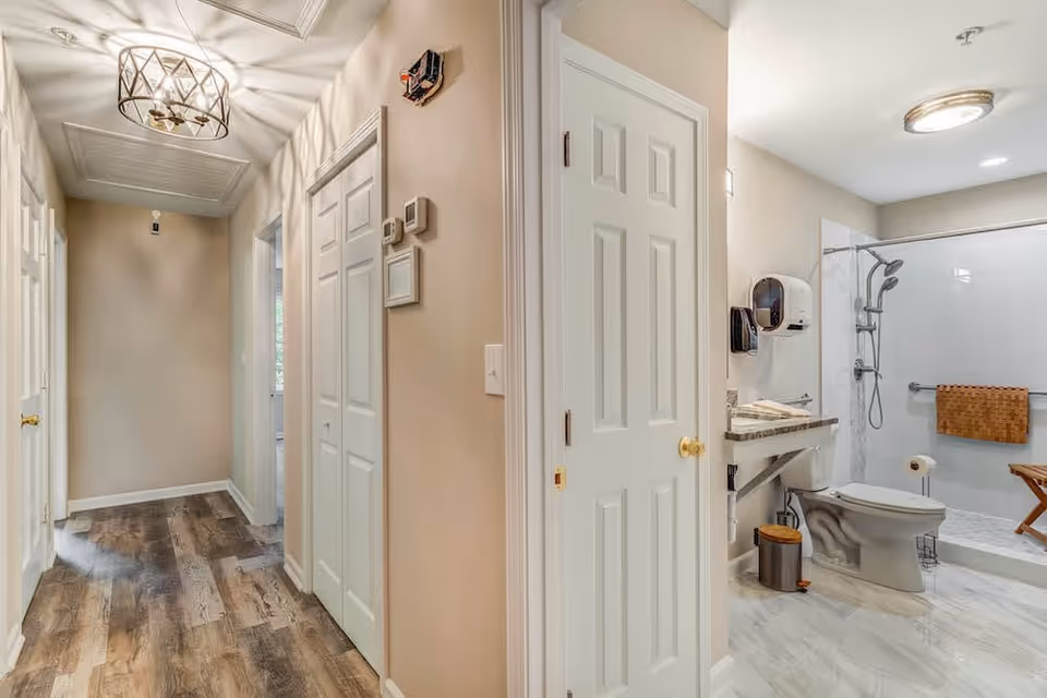 Hallway leading to a modern accessible bathroom with a walk-in shower, toilet, and vanity.