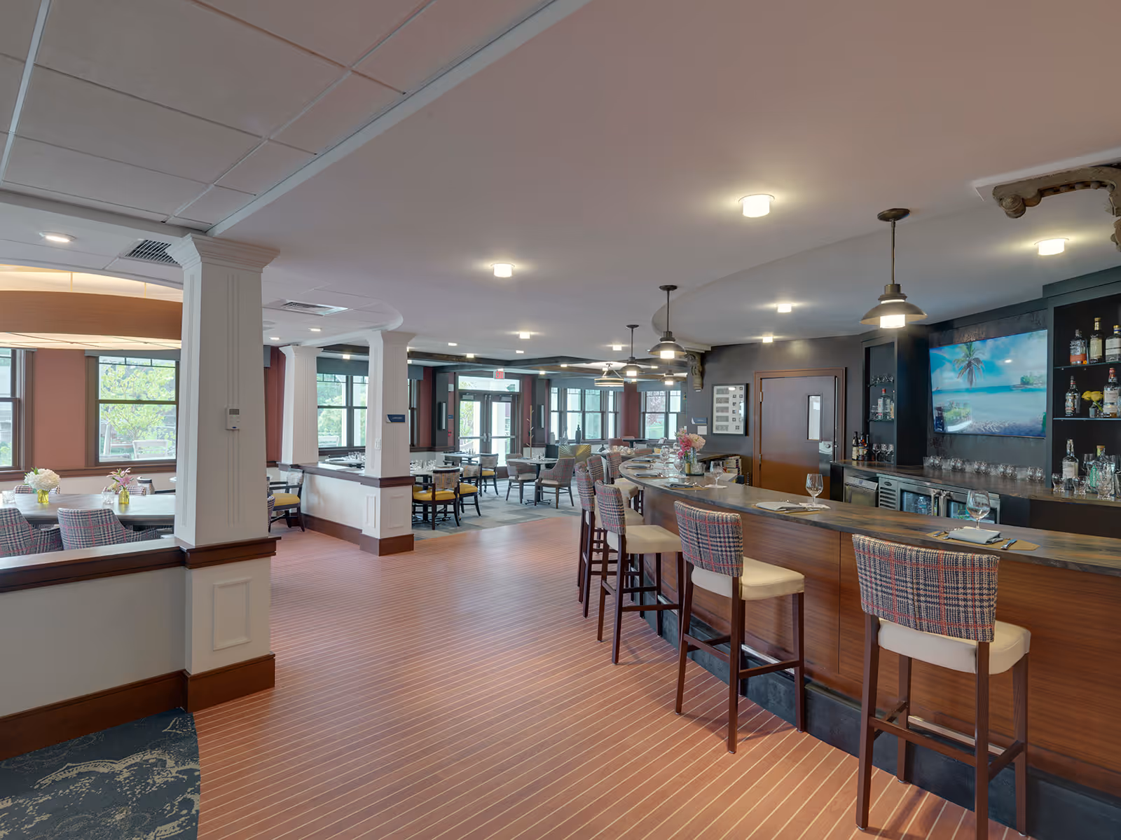 Open dining and bar area with high stools, tables, and large windows in a senior living facility.