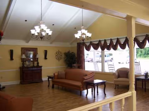 Cozy yellow senior living lounge with orange sofas, chandeliers, and large windows.